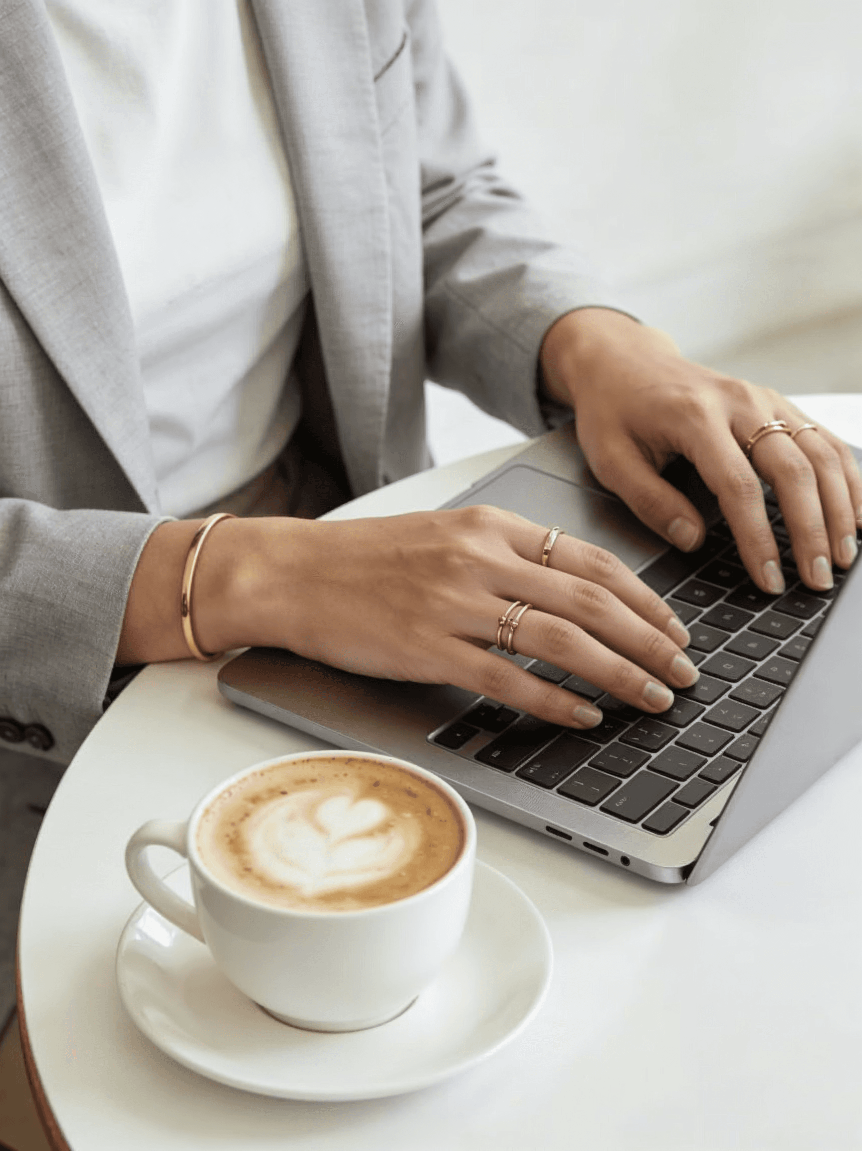 Hands typing on a laptop beside a cappuccino