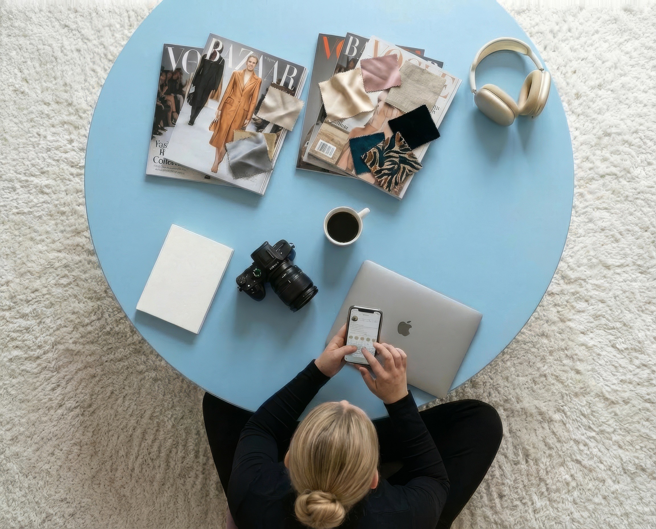 Overhead view of a creator with a phone, camera and magazines on a blue table